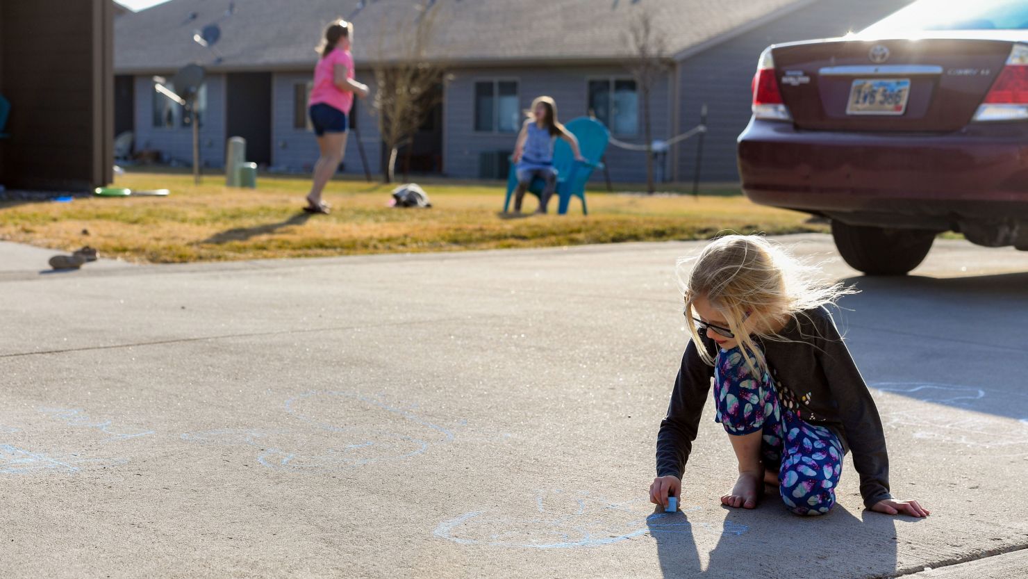 Lexus Larson, age 8, draws with sidewalk chalk outside her house while her friends, Maliah, 10, and Makinley Walsh, 7, play in their own yard across the street on Monday, April 6, in Sioux Falls, South Dakota.