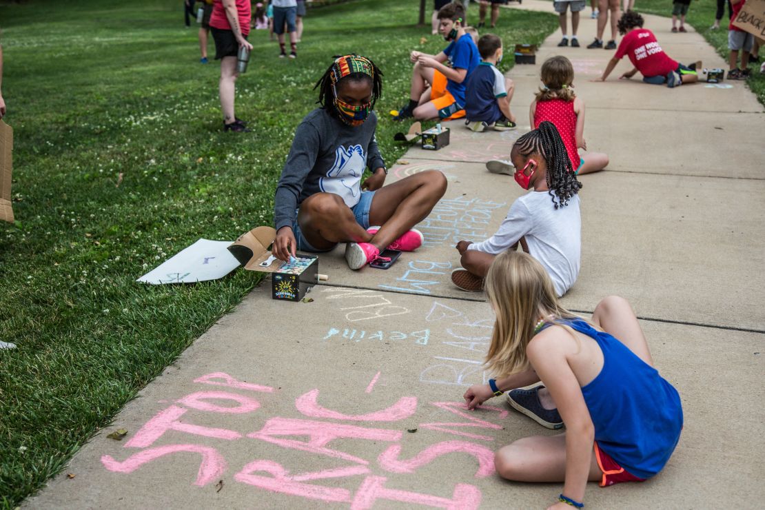 Children writing phrases "Stop Racism" and "Black Lives Matter" on the sidewalk with chalk during the march. 