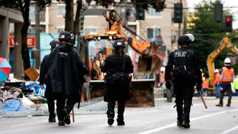 Seattle police walk past debris and bulldozing equipment near the East Precinct on July 1 after police cleared the CHOP.