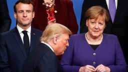 TOPSHOT - France's President Emmanuel Macron (L) and Germany's Chancellor Angela Merkel (R) look at US President Donald Trump (C) walking past them during a family photo as part of the NATO summit at the Grove hotel in Watford, northeast of London on December 4, 2019. 