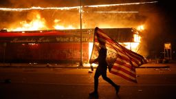 A protester carries a U.S. flag upside down, a sign of distress, next to a burning building Thursday, May 28, 2020, in Minneapolis. Protests over the death of George Floyd, a black man who died in police custody Monday, broke out in Minneapolis for a third straight night. 