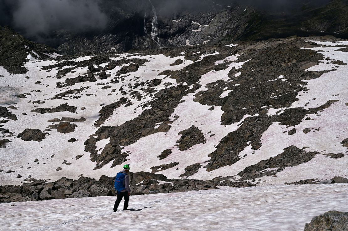 A man is seen walking on pink snow on the glacier.