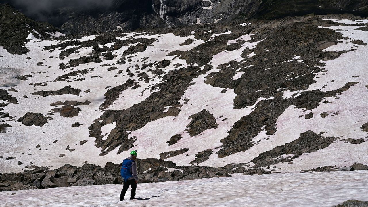 A man is seen walking on pink snow on the glacier.