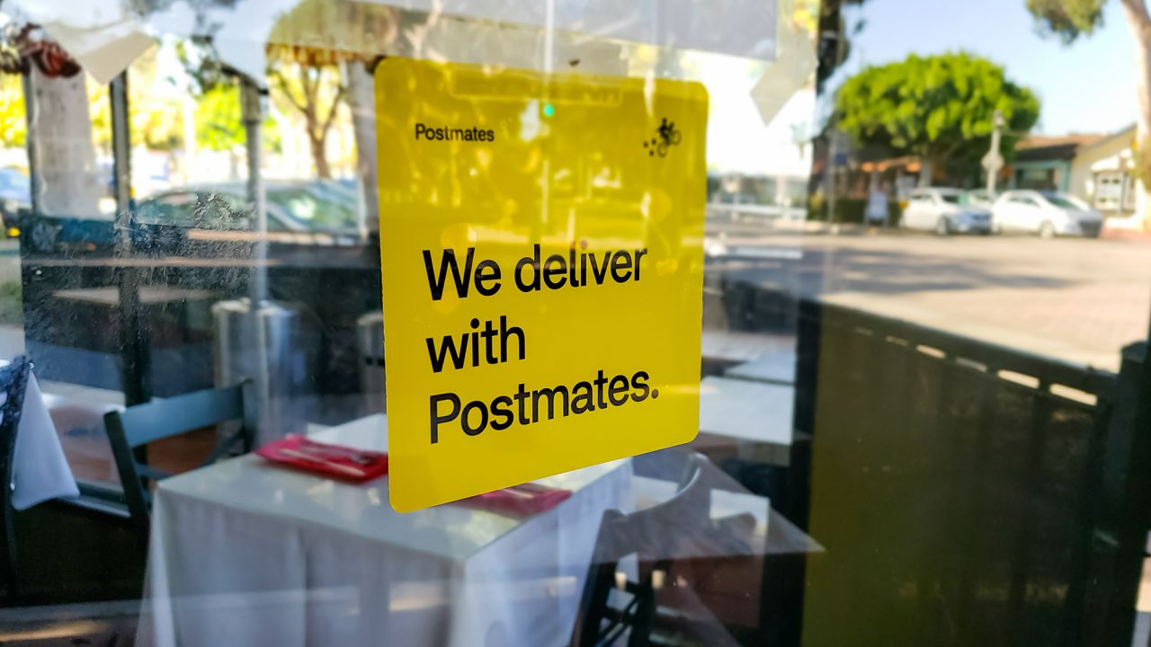 An advertisement sticker on a restaurant window for Postmates, a food delivery app service in Carlsbad, California, in October 2019.