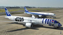 An All Nippon Airways (ANA) Boeing 787-9 aircraft in the livery of Star Wars droid character R2-D2 (front) is seen on the tarmac at Tokyo's Haneda airport on October 14, 2015, as part of the company's Star Wars project. The Boeing aircraft is scheduled to go into service on international routes after a fan