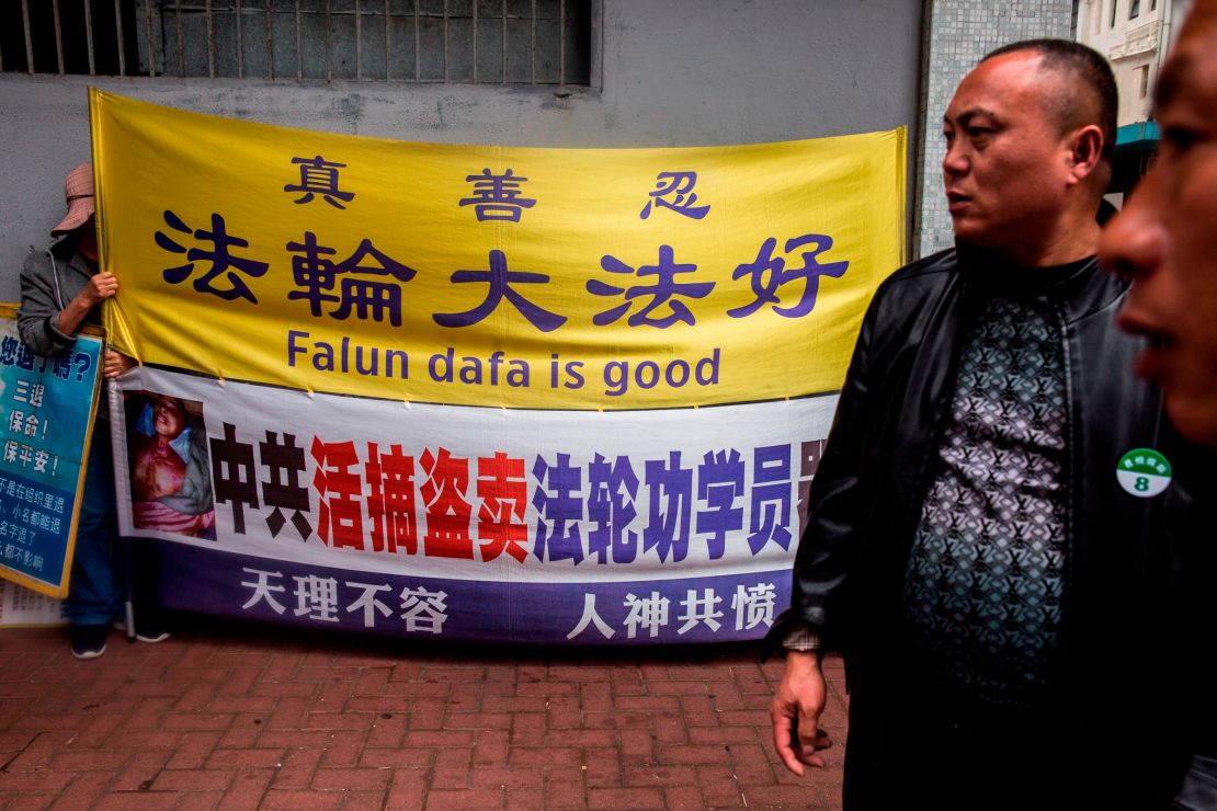 A Falun Gong activist (left) holds a sign next to men from a mailand Chinese tour group in the Kowloon district of Hong Kong on January 6, 2019.