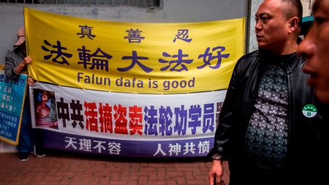 A Falun Gong activist (left) holds a sign next to men from a mailand Chinese tour group in the Kowloon district of Hong Kong on January 6, 2019.