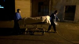 Two Iranian hospital personnel carrying bodies of an Afghan man and an Iranian woman who have died from the new coronavirus disease (COVID-19) by a mobile bed to a morgue in the Firoozabadi hospital in the Shahre-Rey neighborhood in southern Tehran at midnight on June 20, 2020. (Photo by Morteza Nikoubazl/NurPhoto via AP)