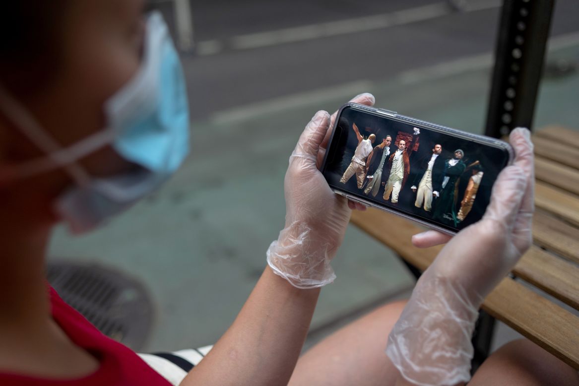 A person watches "Hamilton" on a phone while sitting at an outdoor restaurant in New York City on Friday, July 3. The city recently started Phase Two of its reopening plan, which allows for outdoor dining and the opening of barbershops and salons.