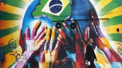 SAO PAULO, BRAZIL - JUNE 10:  A man passes graffiti of multi-colored hands supporting the planet marked with a Brazilian flag on June 10, 2014 in Sao Paulo, Brazil.  The opening match for the 2014 FIFA World Cup is June 12 in Sao Paulo when Brazil takes on Croatia.  (Photo by Mario Tama/Getty Images)