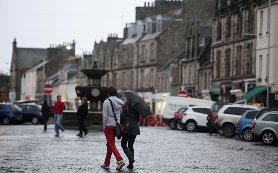 People walk past a fountain in St Andrews, Scotland. 