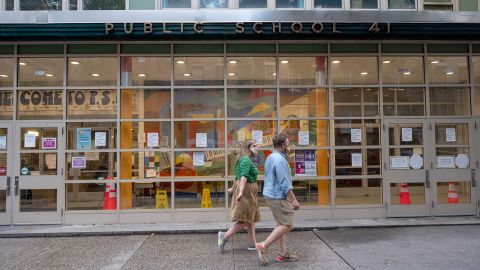 People wearing masks walk past a public school in the Greenwich Village neighborhood of New York City on July 8. Public schools have been closed since March.