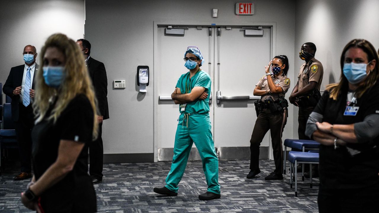Dr. David de la Zerda, center, listens to the governor of Florida during a news conference on coronavirus cases in the state.