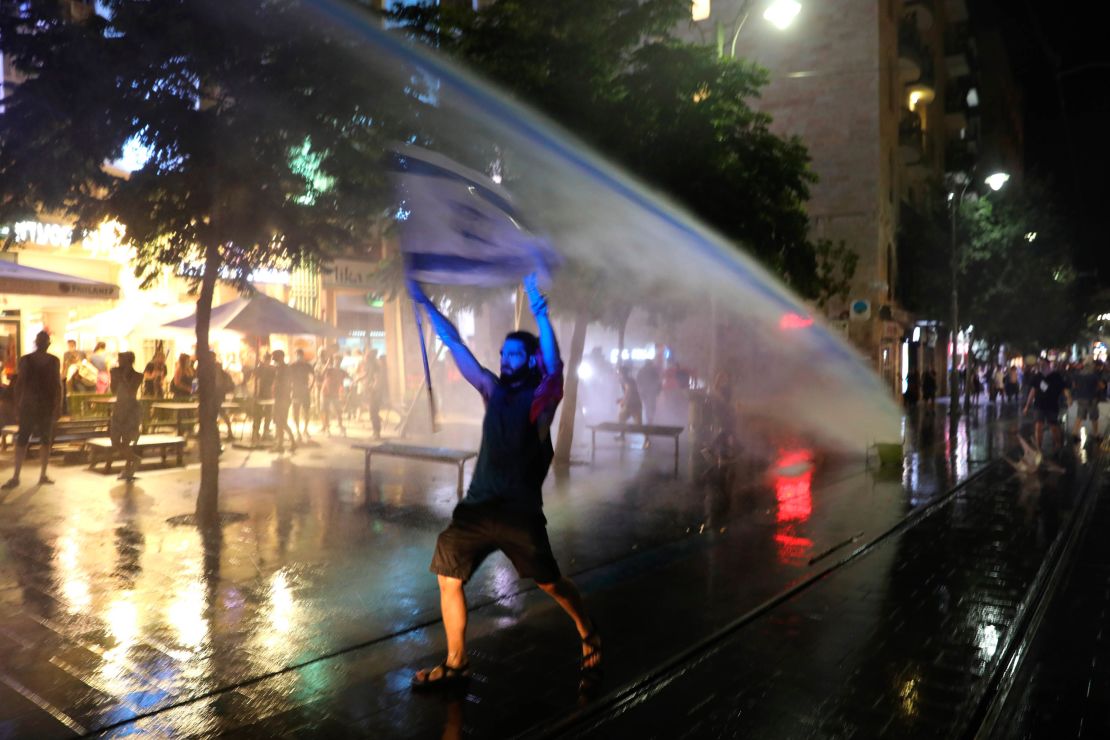 A protester waves an Israeli flag as police use water cannons during clashes at a demonstration against the Israeli prime minister in Jerusalem on Tuesday. 