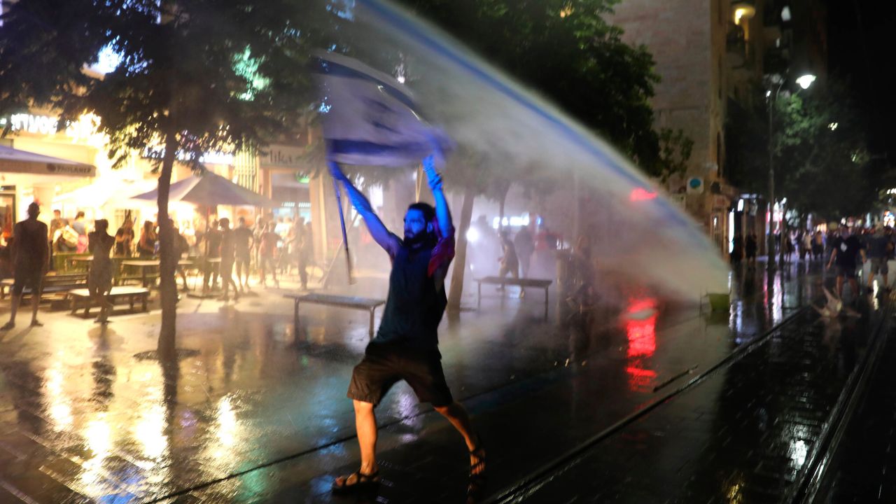 A protester waves an Israeli flag as police use water cannons during clashes at a demonstration against the Israeli prime minister in Jerusalem on Tuesday.
