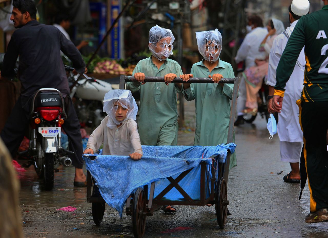 Children cover their faces with plastic bags while pushing a handcart in rainy Peshawar, Pakistan, on Sunday, July 12.