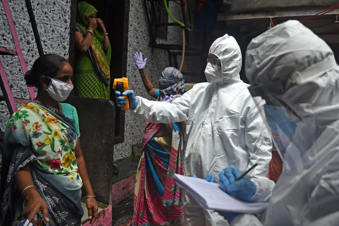 Medical volunteers wearing Personal Protective Equipment (PPE) gear take temperature reading of a woman inside Dharavi slum in Mumbai on July 9, 2020. 