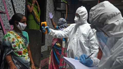 Medical volunteers wearing Personal Protective Equipment (PPE) gear take temperature reading of a woman inside Dharavi slum in Mumbai on July 9, 2020. 