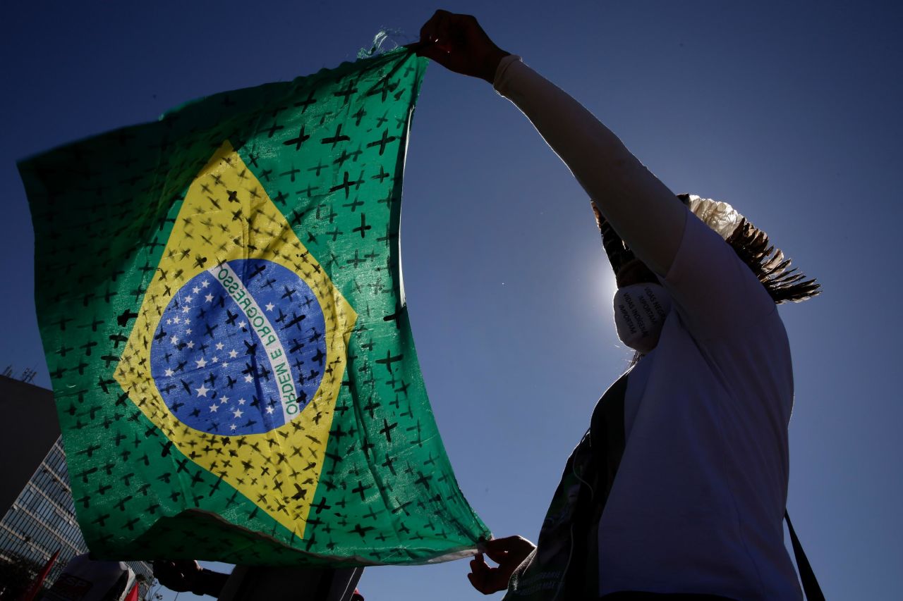 During a protest calling for Bolsonaro to be impeached, a demonstrator holds a Brazilian flag painted with crosses that symbolize thousands of coronavirus deaths.