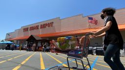 A shopper wearing a facemask pushes her cart while people wait in line to enter The Home Depot in Marina Del Rey, California on May 22, 2020, amid the novel coronavirus pandemic. (Photo by Chris Delmas/AFP/Getty Images)