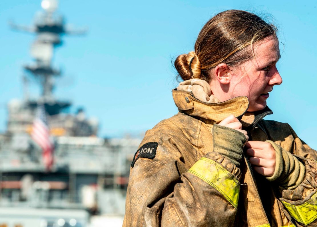 A sailor takes off her firefighting ensemble after combating a fire aboard the amphibious assault ship USS Bonhomme Richard.