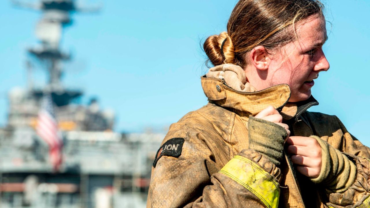 A sailor takes off her firefighting ensemble after combating a fire aboard the amphibious assault ship USS Bonhomme Richard.