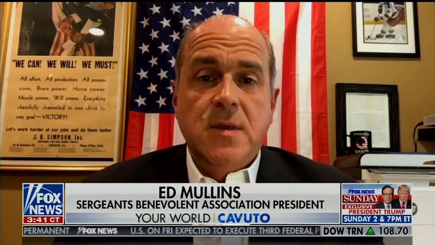 Ed Mullins during an appearance on Fox News Friday. A coffee mug with the logo of QAnon sits above his left shoulder in the bottom right of the photo.