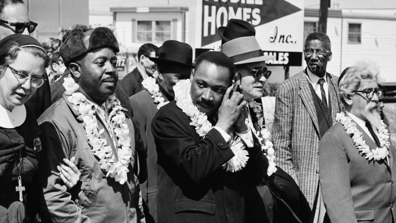 Martin Luther King, Jr. listening to a transistor radio on a march from Selma to Montgomery, Alabama, on March 23, 1965. Among the other marchers was Rabbi Abraham Joshua Heschel, far right.
