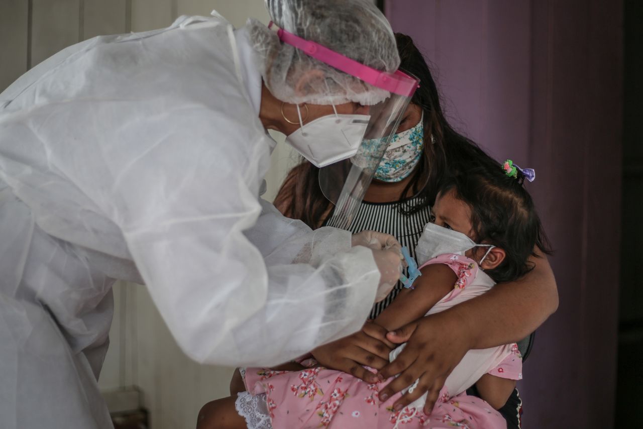 <strong>Brazil:</strong> A mother holds her daughter while a nurse wearing a protective mask and shield gives the child a flu vaccine. 