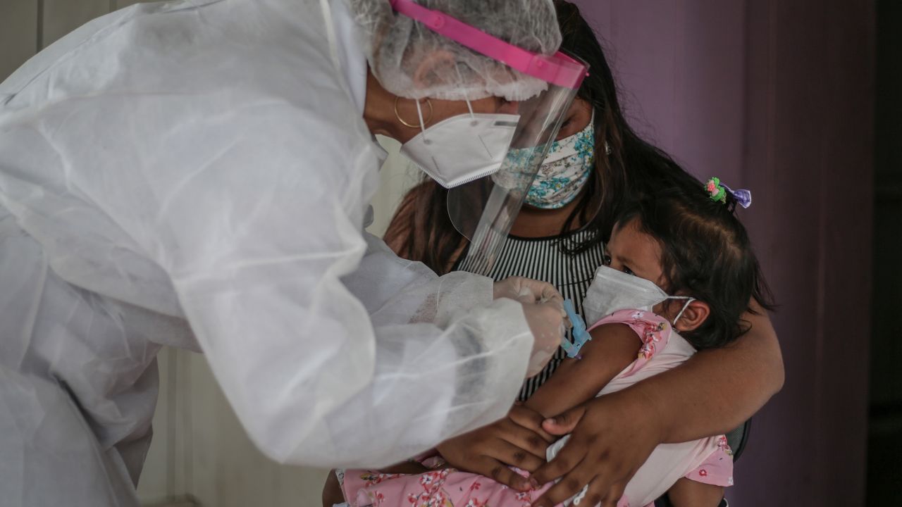 A mother in Brazil holds her daughter while a nurse gives her a flu vaccine. 