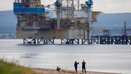 Pedestrians walk along a beach in view of the Noble Sam Turner jack-up drilling rig, operated by Noble Corp., in the Port of Cromarty Firth in Cromarty, U.K., on Tuesday, June 23, 2020. Oil headed for a weekly decline -- only the second since April -- as a surge in U.S. coronavirus cases clouded the demand outlook, though the pessimism was tempered by huge cuts to Russia's seaborne crude exports. Photographer: Jason Alden/Bloomberg via Getty Images