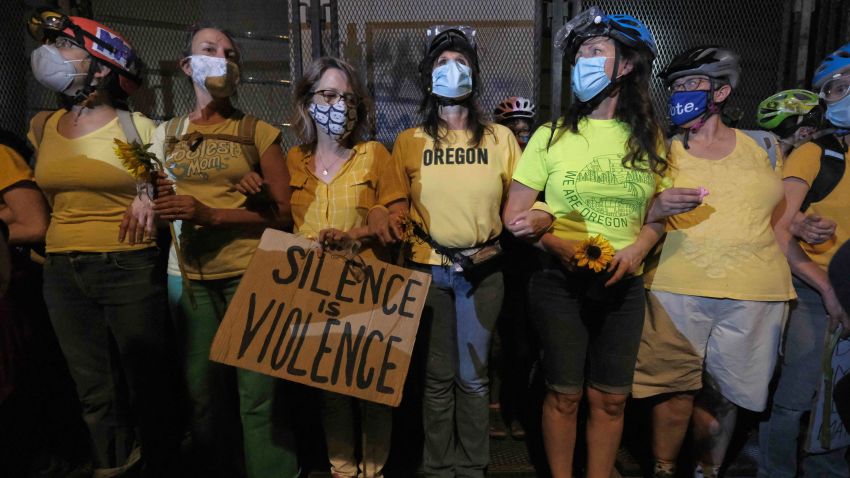 Women with interlocking arms stand with their backs up against a fence blocking access to the entrance of the federal courthouse in Portland, Ore., on July 19, 2020. (Photo by Alex Milan Tracy/Sipa USA)(Sipa via AP Images)