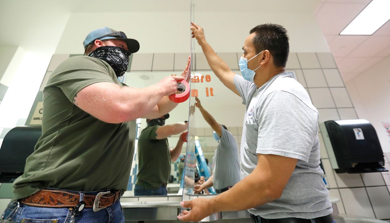 School workers Matt Attaway, left, and Rogelio Ponciano install a Plexiglas barrier in a restroom at Bukhair Elementary School in Dallas on July 15.