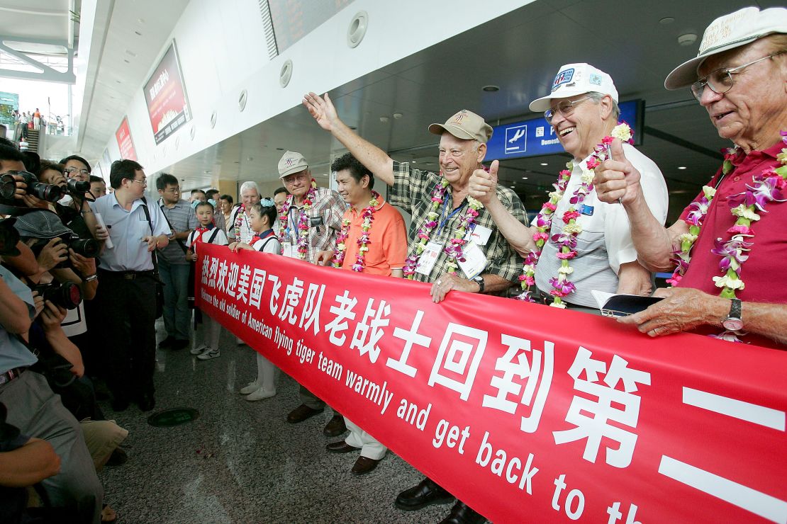 US World War II veterans, including former Flying Tigers, pose for pictures with a banner as a cheering crowd welcome them at the Chongqing Jiangbei Airport on August 18, 2005.