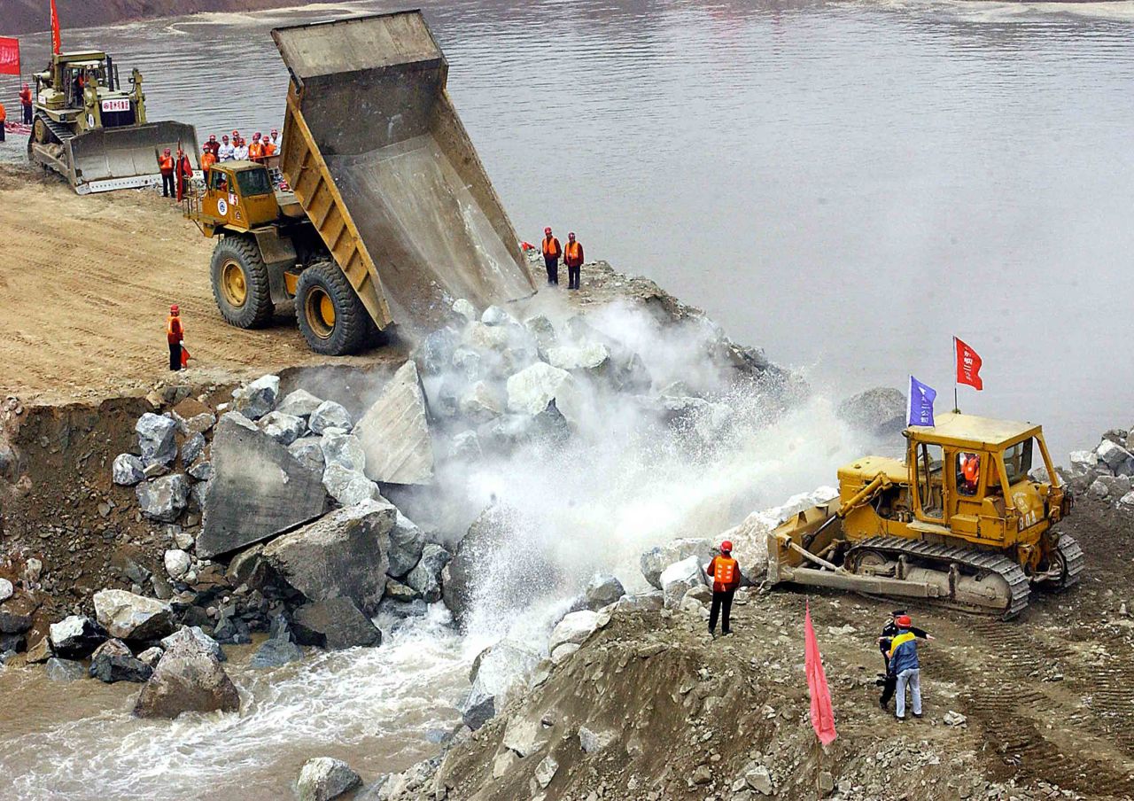 Trucks dump rocks across the last remaining section of a diversion canal linked to the Yangtze river, as workers prepare to dam the Yangtze on November 6, 2002.