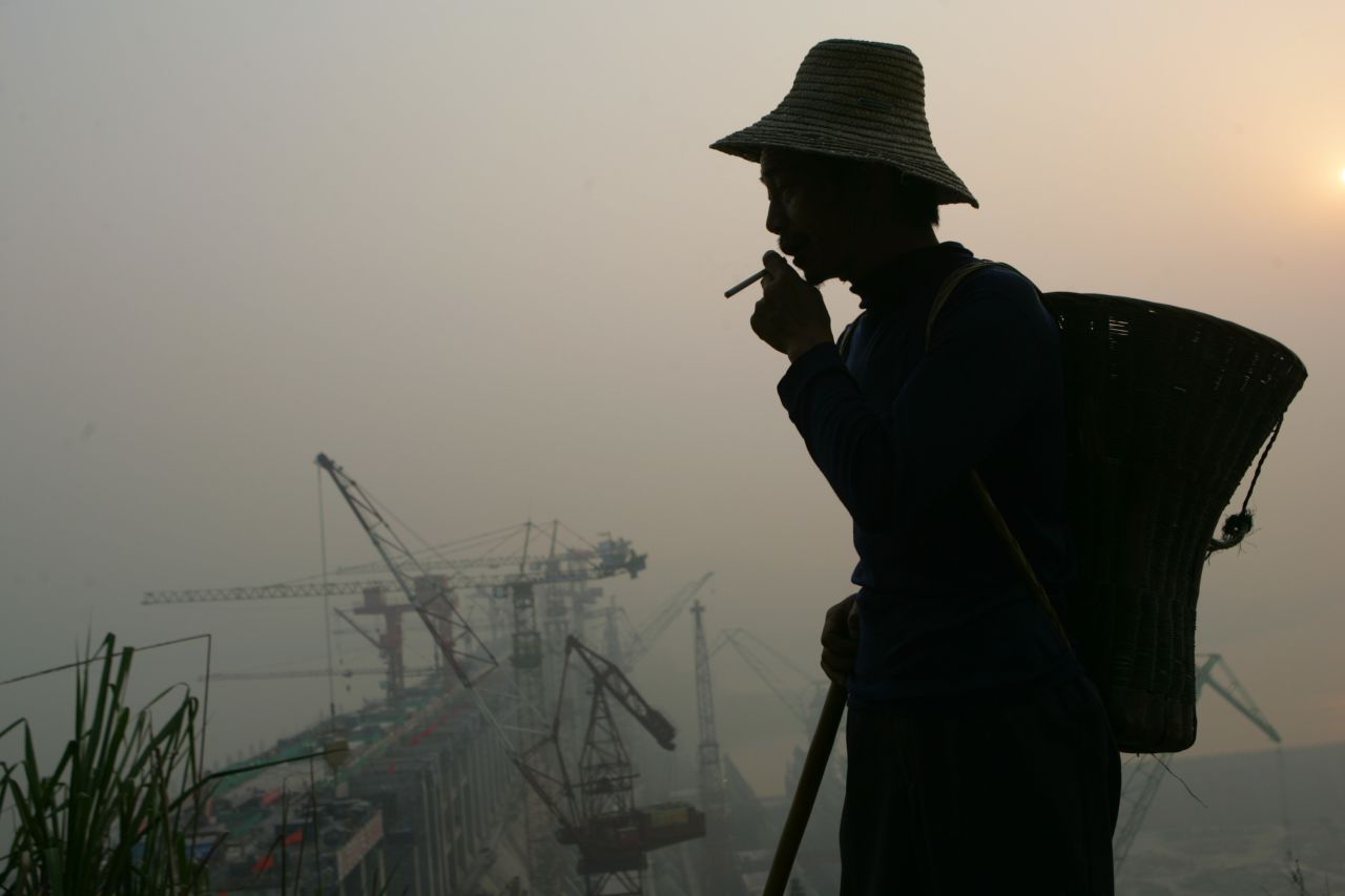 A farmer watches as workers carry out construction on the final part of the main body of the Three Gorges Dam on May 19, 2006.