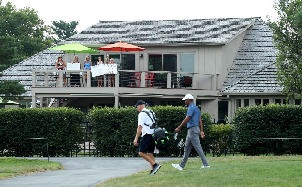 Behind closed doors: Tiger Woods walks past fans looking on from a nearby house on the 17th hole during the second round of the Memorial tournament on July 17, 2020 at Muirfield Village Golf Club in Dublin, Ohio. Since the PGA Tour returned to action in June, there have been spectator-free tournaments in Texas, South Carolina, Connecticut and Michigan. The Memorial event was also closed to the general public.