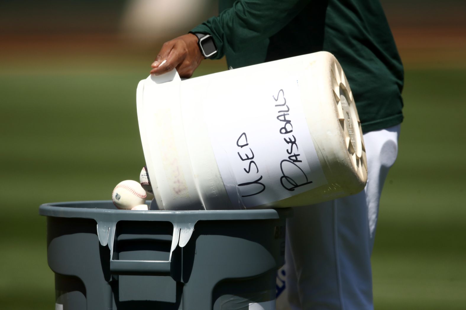 A coach dumps a bucket of used baseballs during workouts in Oakland on July 5. During the season, balls will be taken out of play after they've been handled by multiple players. Then the balls will be sanitized and recycled days later.