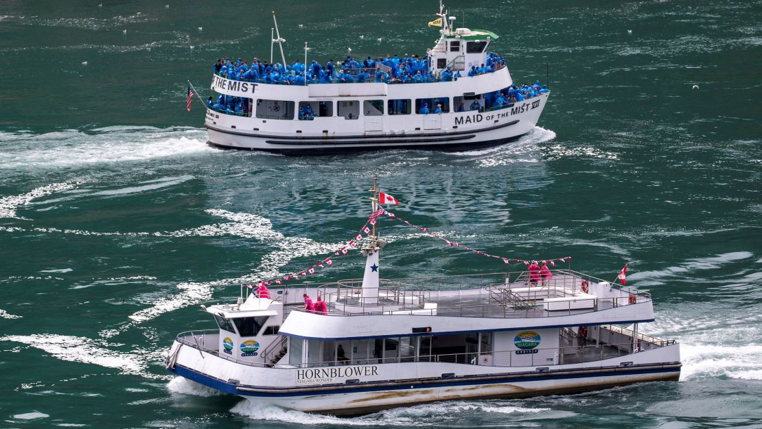 A people-laden tour boat operated by US company Maid of the Mist sails past a sparsely populated boat run by Canada's Hornblower Niagara Cruises.