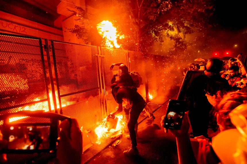 Protesters throw flaming debris over a fence at the Mark O. Hatfield United States Courthouse on Wednesday, July 22, 2020, in Portland, Ore. Following a larger Black Lives Matter Rally, several hundred demonstrators faced off against federal officers at the courthouse. (AP Photo/Noah Berger)