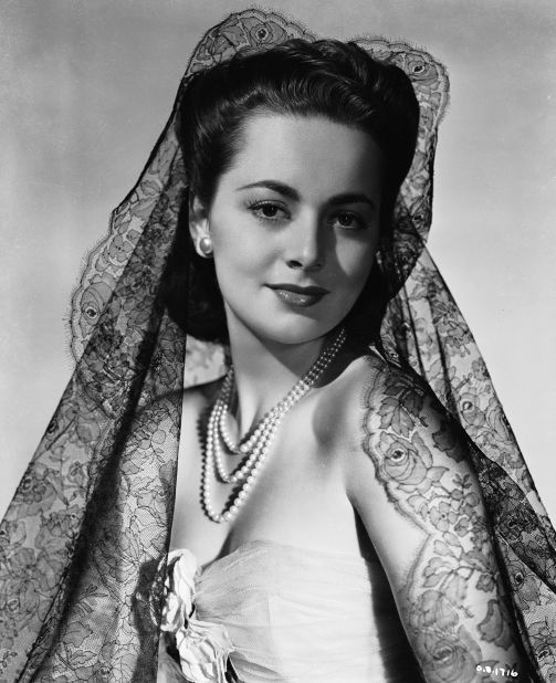 While many of her outfits can be credited to the costume designers she worked with, de Havilland also owned a large collection of designer clothes. Here she is pictured wearing a black lace veil and pearl necklace (circa 1940). 