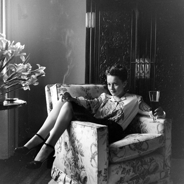 The actress is pictured relaxing at home, holding a lit cigarette and glass of beer, the embodiment of the modern woman. On her feet she wears a towering pair of thick-heeled Mary Janes.