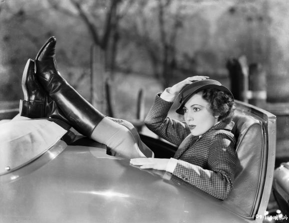 The actress is captured in a blazer and tall leather boots at the back of a convertible in 1936.