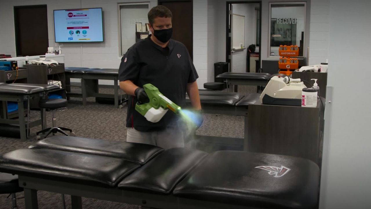 An Atlanta Falcons staff member uses an electrostatic sprayer to disinfect a training table.