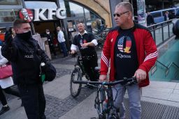 A policeman instructs men wearing QAnon conspiracy shirts to move along during protests against the coronavirus lockdown at Alexanderplatz in Berlin, Germany, on May 16, 2020.