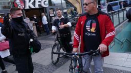 A policeman instructs men wearing QAnon conspiracy shirts to move along during scattered protests at Alexanderplatz against lockdown measures and other government policies relating to the novel coronavirus crisis on May 16, 2020 in Berlin, Germany. 