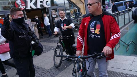 A policeman instructs men wearing QAnon conspiracy shirts to move along during protests against the coronavirus lockdown at Alexanderplatz in Berlin, Germany, on May 16, 2020.