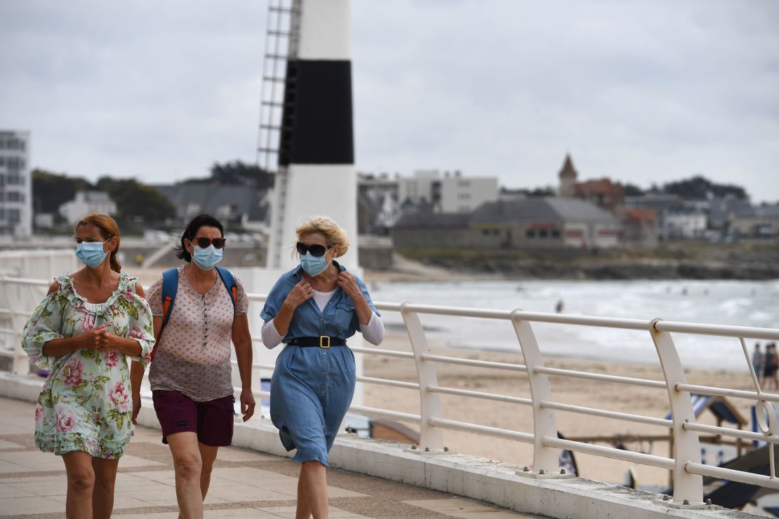 Women wearing masks walk along the seafront in Quiberon after a nighttime curfew was imposed on local beaches.