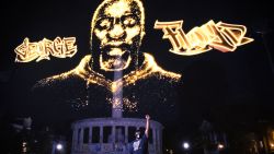 Rdoney Floyd stands in front of a hologram honoring his brother as it is projected over the Robert E. Lee statue in Richmond, Virginia, during a private event on July 27.  CNN obscured portions graffiti on the statue that contained profanity. 