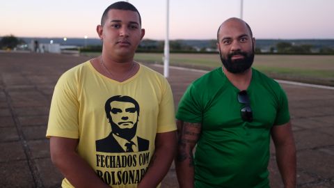 Supporters of President Bolsonaro gather outside his residence. One wears a t-shirt that reads "Sticking with Bolsonaro" on the front and "All power to the people" on the back.
